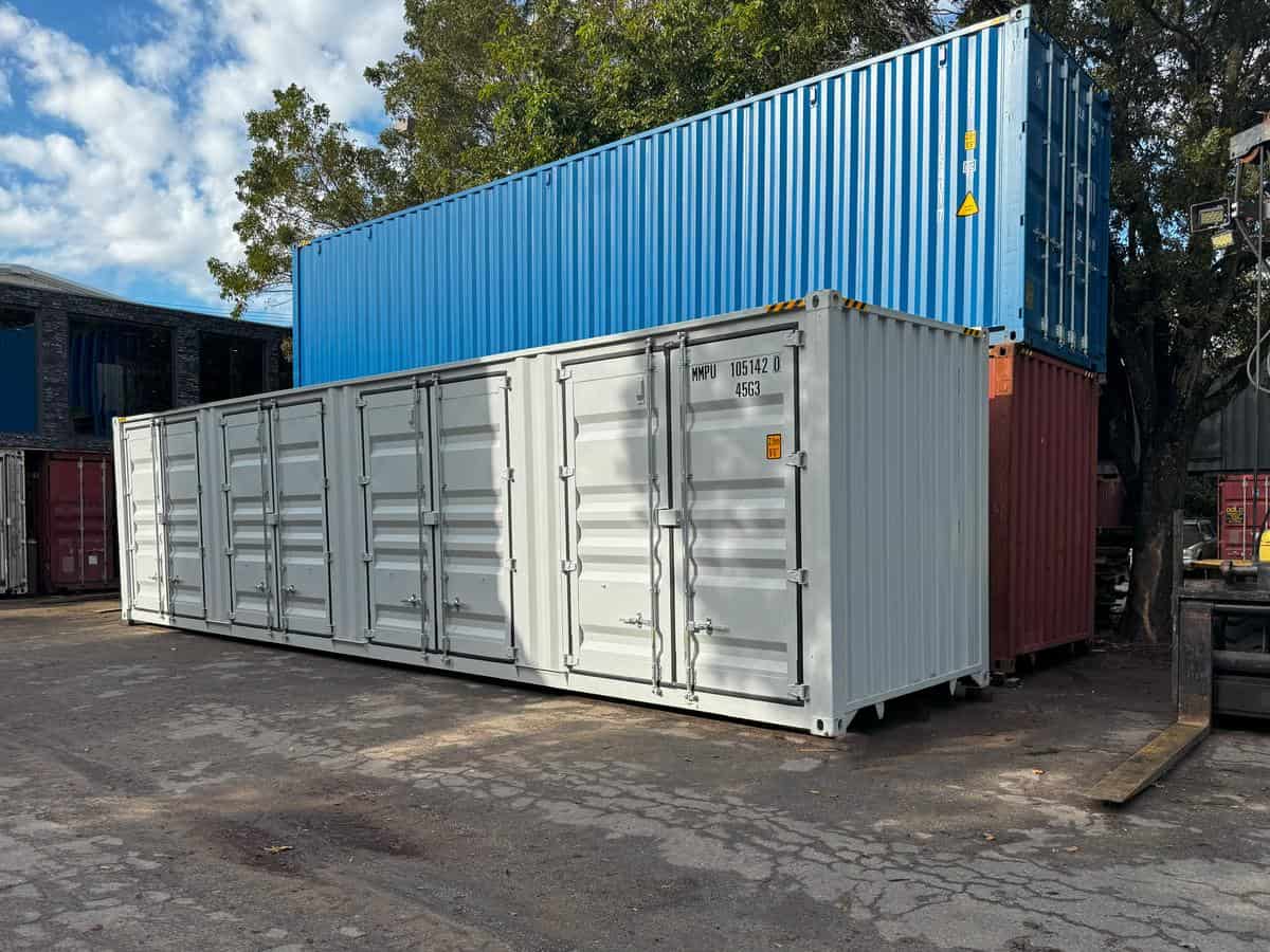 A long, white, open-side shipping container, featuring eight large, segmented side-opening double doors running along its entire length. 